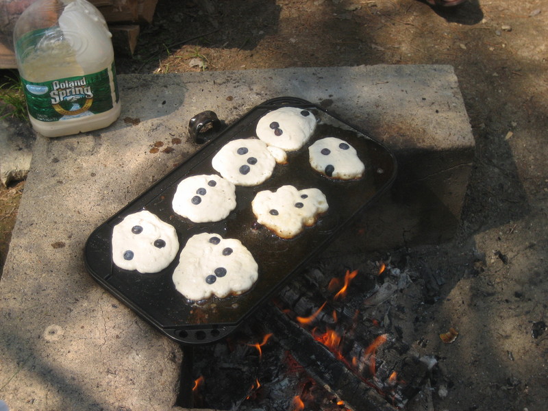 Blueberry pancakes on a griddle on a camp fire.